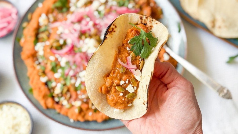 Holding a corn tortilla filled with refried Mayocoba beans