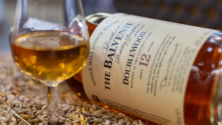 A glass and bottle of The Balvenie DoubleWood 12 Year on a bed of grains