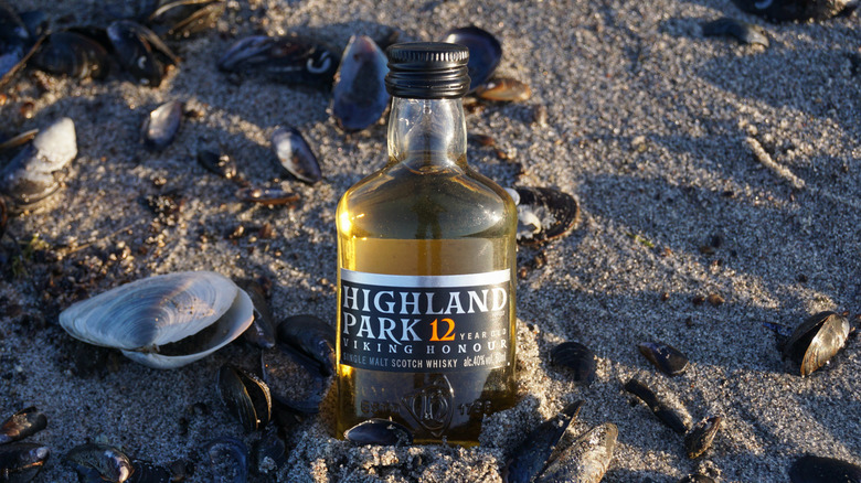 A bottle of Highland Park 12 Year on a sandy beach with shells