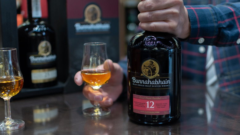Hand holding the top of a bottle of Bunnahabhain 12 Year with a neat pour in a glass