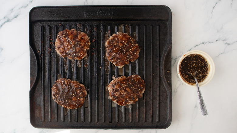 Grilled pork patties on a grill pan glazed in a dark sauce