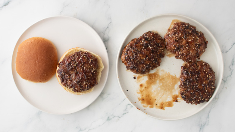 A glazed pork patty on a burger bun next to pork patties on plate
