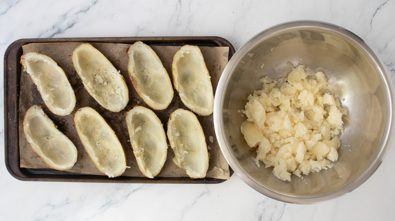 A baking sheet containing potato skins and a large bowl containing the potato flesh
