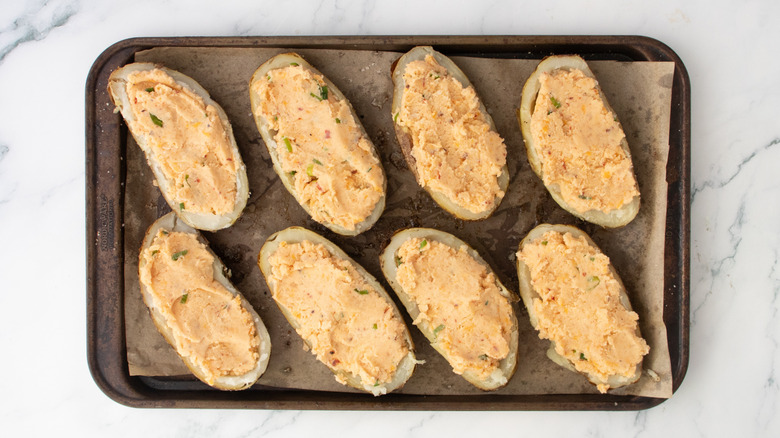 Potato skins on a large baking sheet filled with seasoned mashed potato