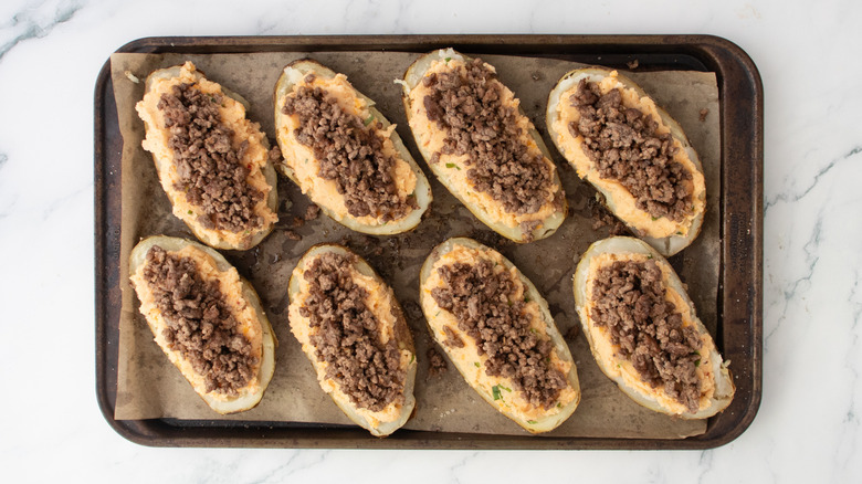 Potato skins on a large baking sheet filled with seasoned mashed potato and taco beef