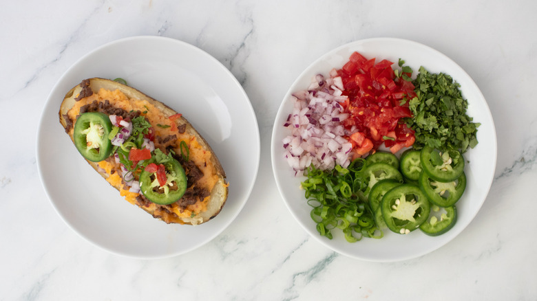 A plated taco-themed twice baked topped with tomatoes, jalapeños, onions, and herbs