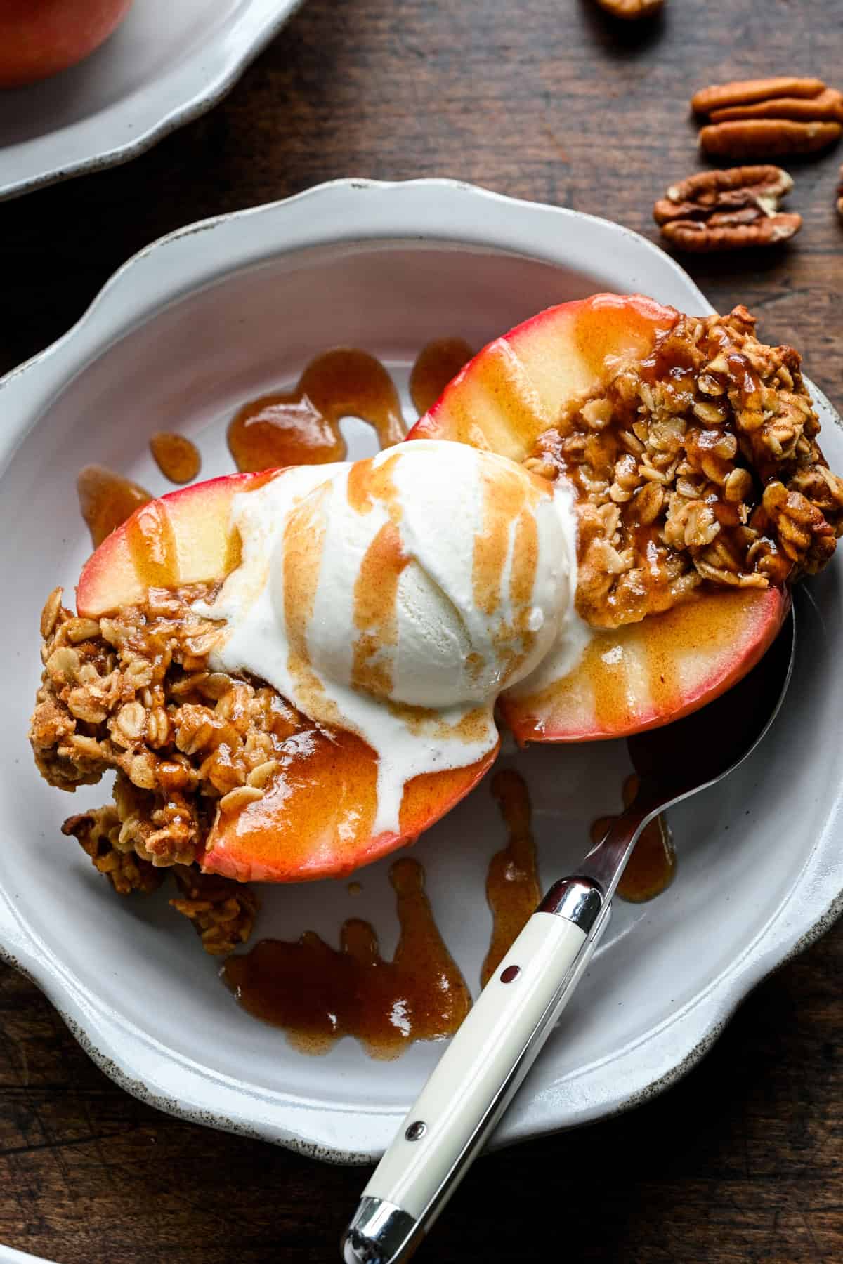 Close view of a baked apple split open, vanilla ice cream melting into the oat crumble with date caramel pooling on the plate.