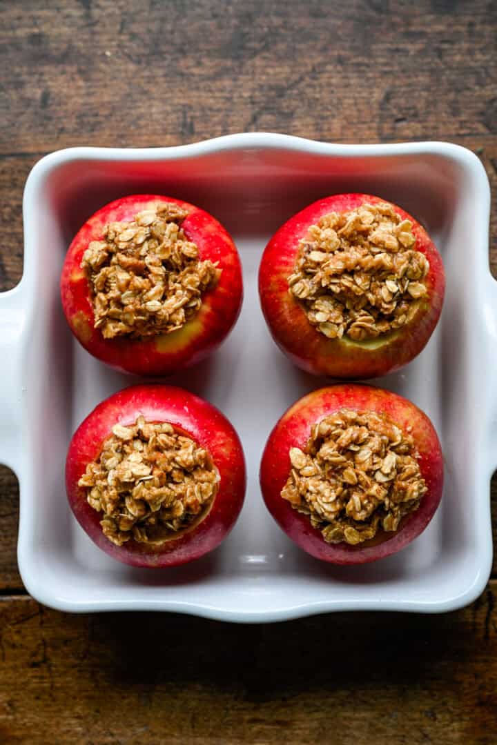 Cored apples packed with oat crumble filling in a white baking dish before baking.