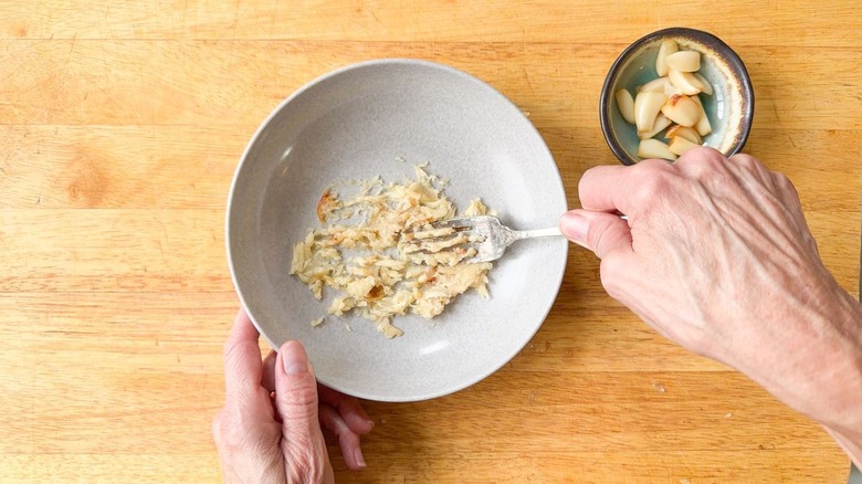 Mashing roasted garlic cloves into a paste with a fork in a small bowl