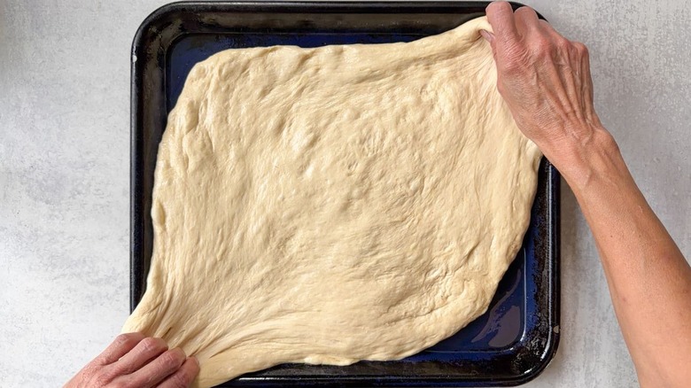 Stretching focaccia dough over oiled blue baking sheet