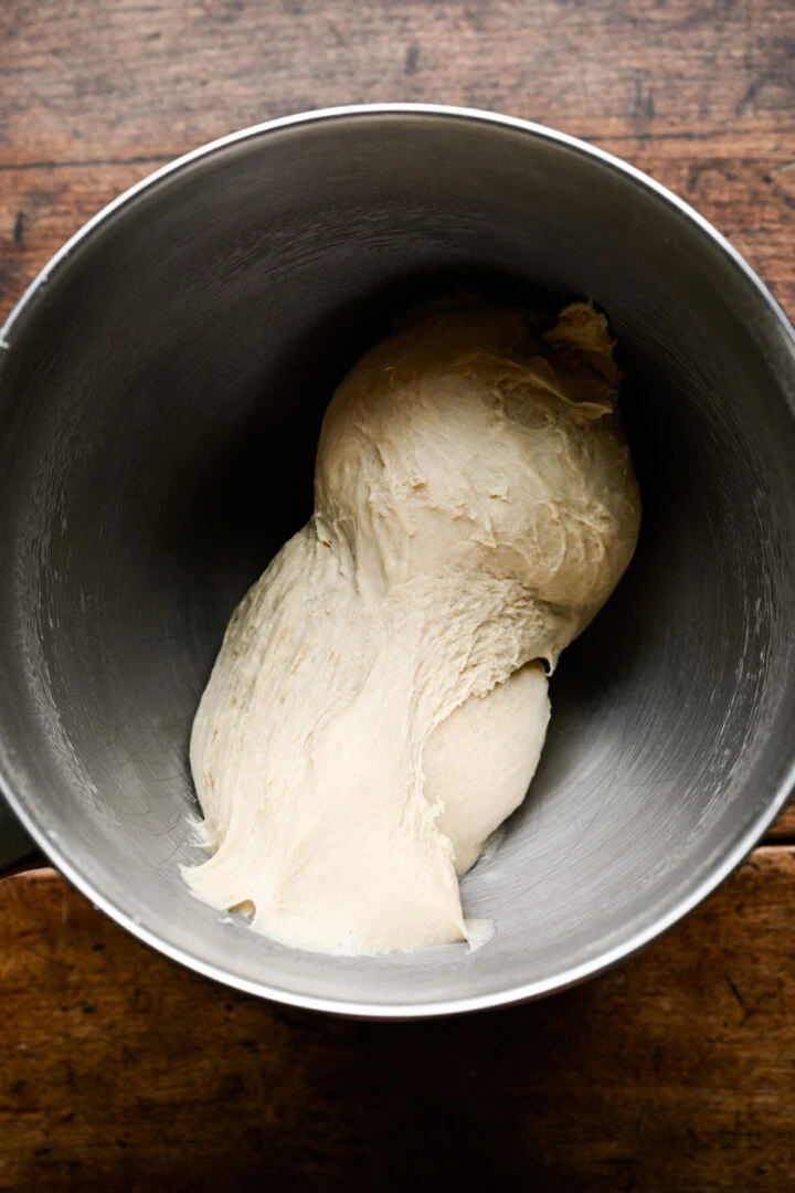 Soft, stretchy pretzel dough starting to come together in a stainless steel mixer bowl.