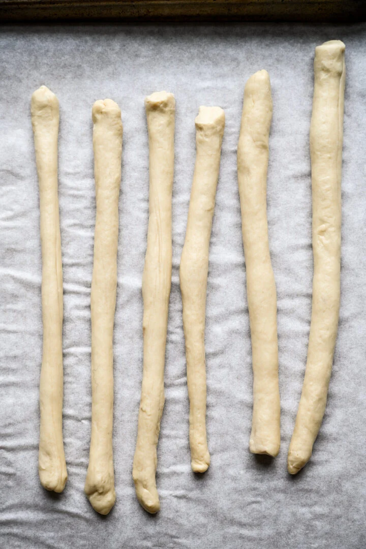 Six long ropes of pretzel dough rolled out side by side on parchment paper.