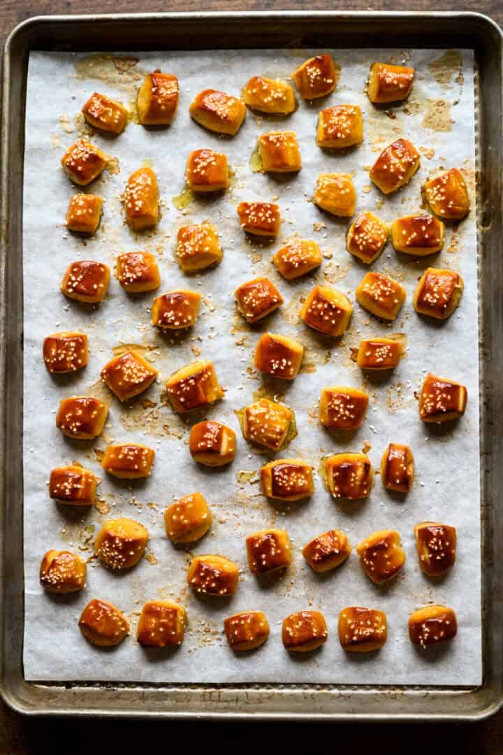 Overhead view of shiny, deep golden-brown pretzel bites with pretzel salt, spaced out in rows on a parchment-lined sheet pan.
