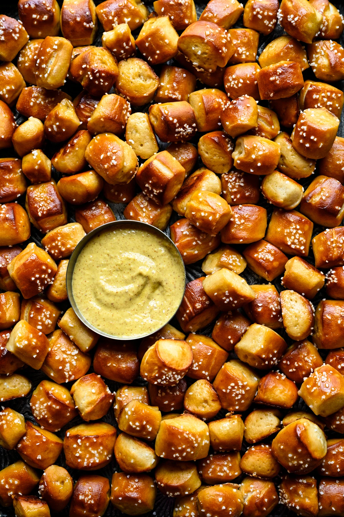 Close overhead view of a pile of buttery soft pretzel bites with pretzel salt surrounding a small bowl of mustard dip.