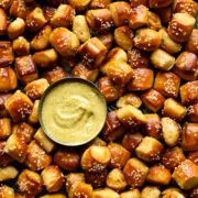Close overhead view of a pile of buttery soft pretzel bites with pretzel salt surrounding a small bowl of mustard dip.