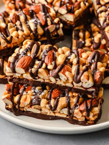 Close up view of dark chocolate and sea salt nut bars stacked on a white plate.