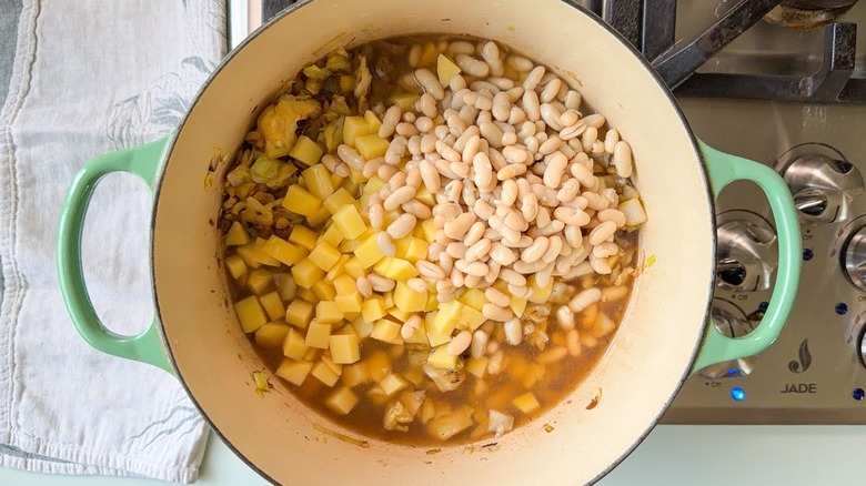 White beans, diced yellow potatoes, vegetable stock, and chopped charred cabbage in Dutch oven on stovetop