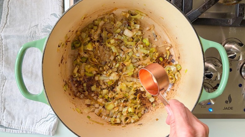 Adding white vermouth to Dutch oven with sautéed leeks and spices on stovetop