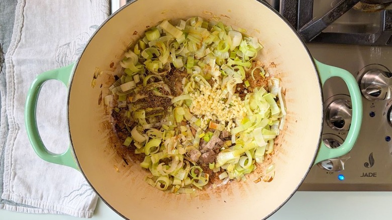 Sliced leeks with chopped garlic and spices in Dutch oven on stovetop