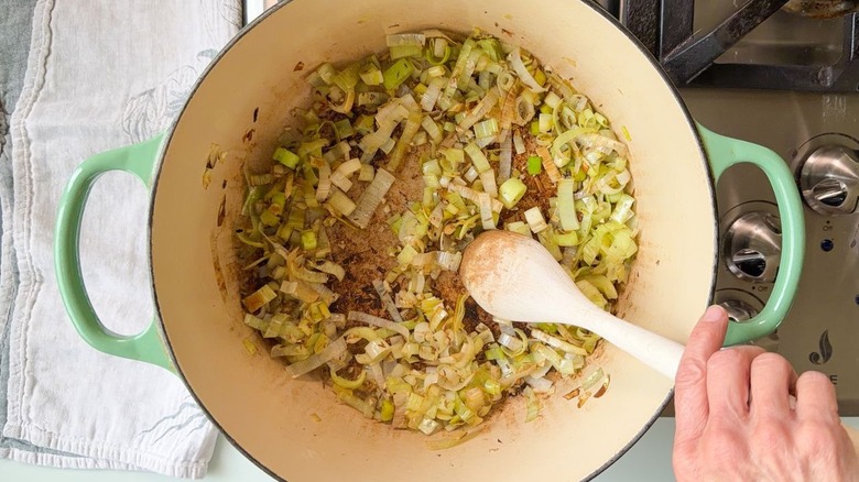 Stirring sliced leeks with chopped garlic and spices in green Dutch oven on stovetop