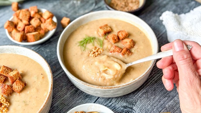 Spooning vegan Nordic-style creamy cabbage soup with rye croutons, dill, and mustard seeds from serving bowl
