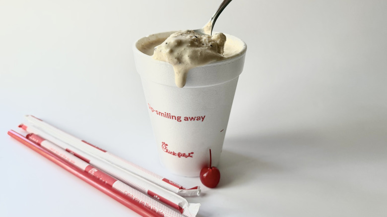 Chick-fil-A's S'mores Milkshake with a spoon inserted into the cup next to a cherry, straws, and the lid