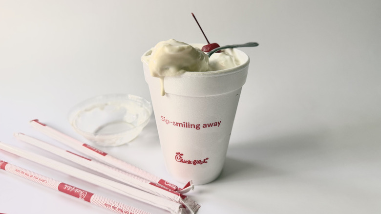 Chick-fil-A's Vanilla Milkshake with a spoon on the cup next to a cherry, straws, and the lid