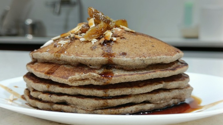 A stack of buckwheat cakes on a plate with syrup drizzled all over them.