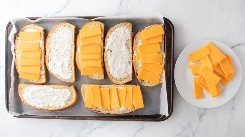 A large baking sheet with four bread slices containing slices of cheddar cheese.