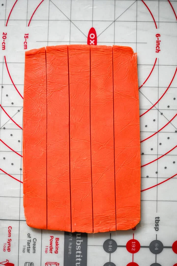 A rectangle of orange dough on a measuring mat, cut lengthwise into five even strips.
