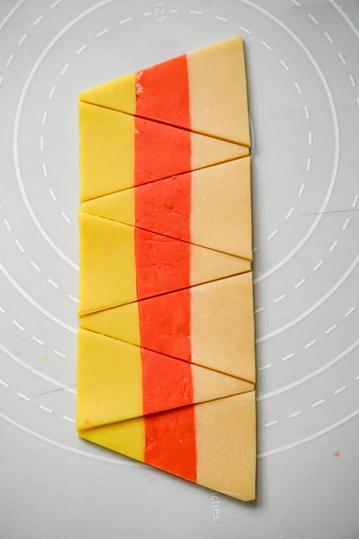 A striped strip of yellow, orange and plain dough cut into alternating candy corn triangles.