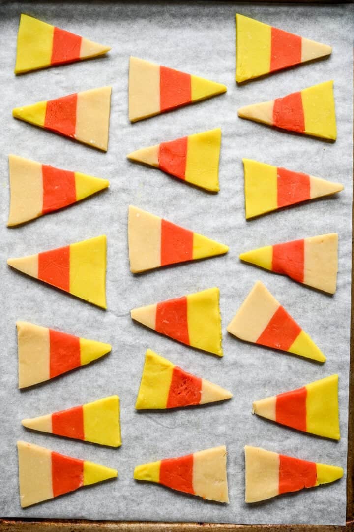 Unbaked candy corn cookie triangles spaced out on a parchment-lined sheet pan.