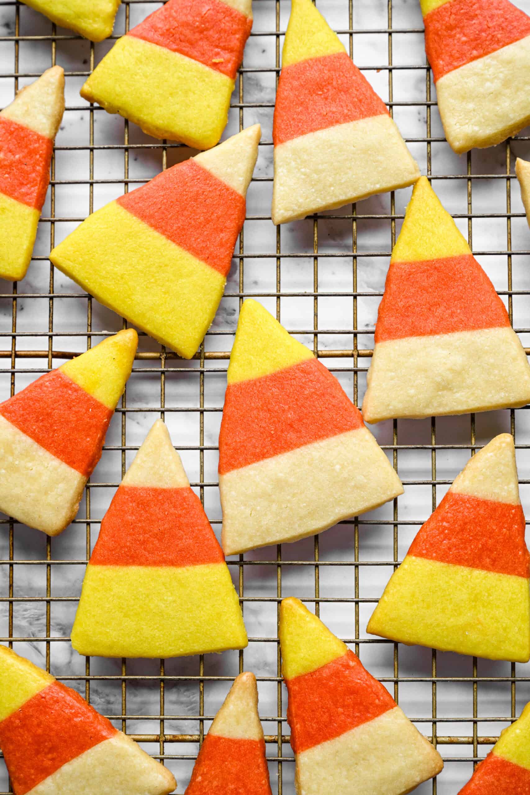 Close-up of baked candy corn shortbread cookies on a wire cooling rack, each a triangle with yellow, orange and white stripes.