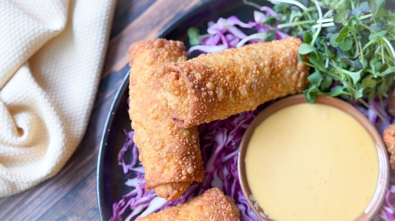 Crab cake egg rolls on serving plate with lemon-soy aioli dipping sauce and shredded purple cabbage