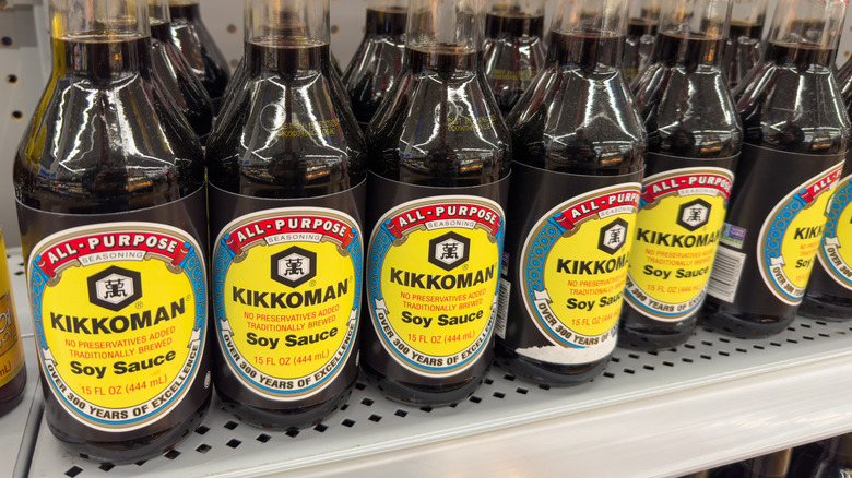 Bottles of Kikkoman soy sauce lined up on a store shelf.
