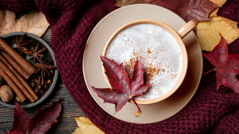 A maple latte is photographed from above, with spices and leaves on the side.