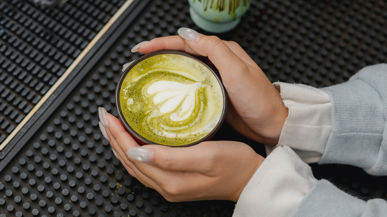 A person's hands are seen cupping a matcha latte.