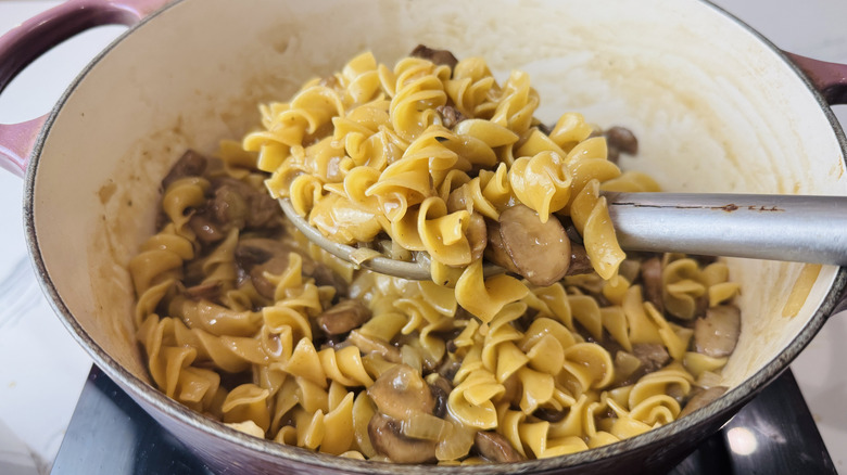 Scoop removing noodles and mushrooms from pot
