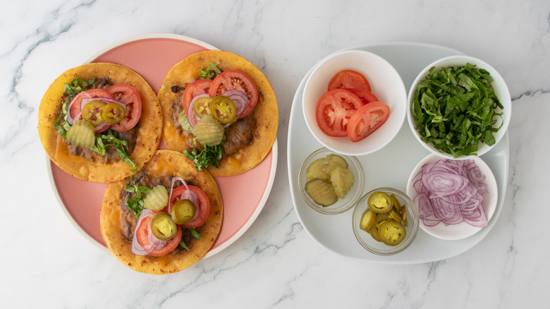 A plate filled with burger tacos topped with fresh and pickled ingredients