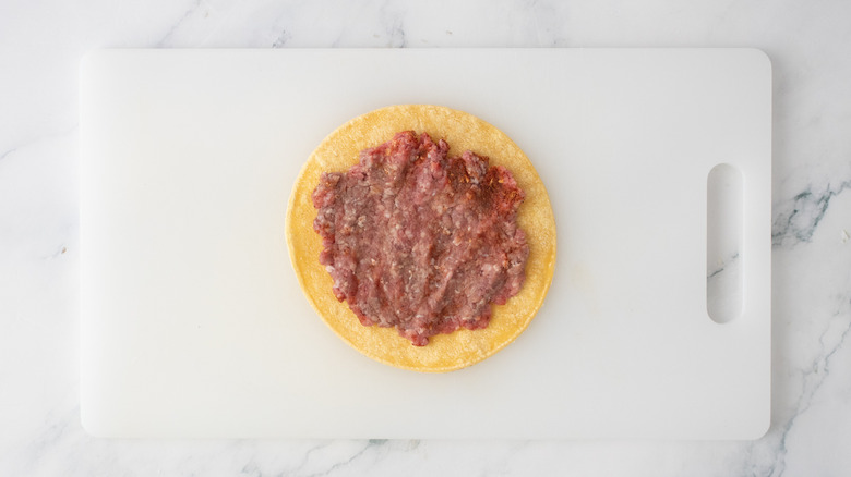 A corn tortilla with a smashed burger patty on top