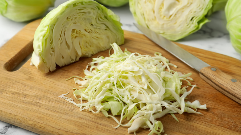 Half a cabbage and some long strips of chopped cabbage on wooden board with a knife
