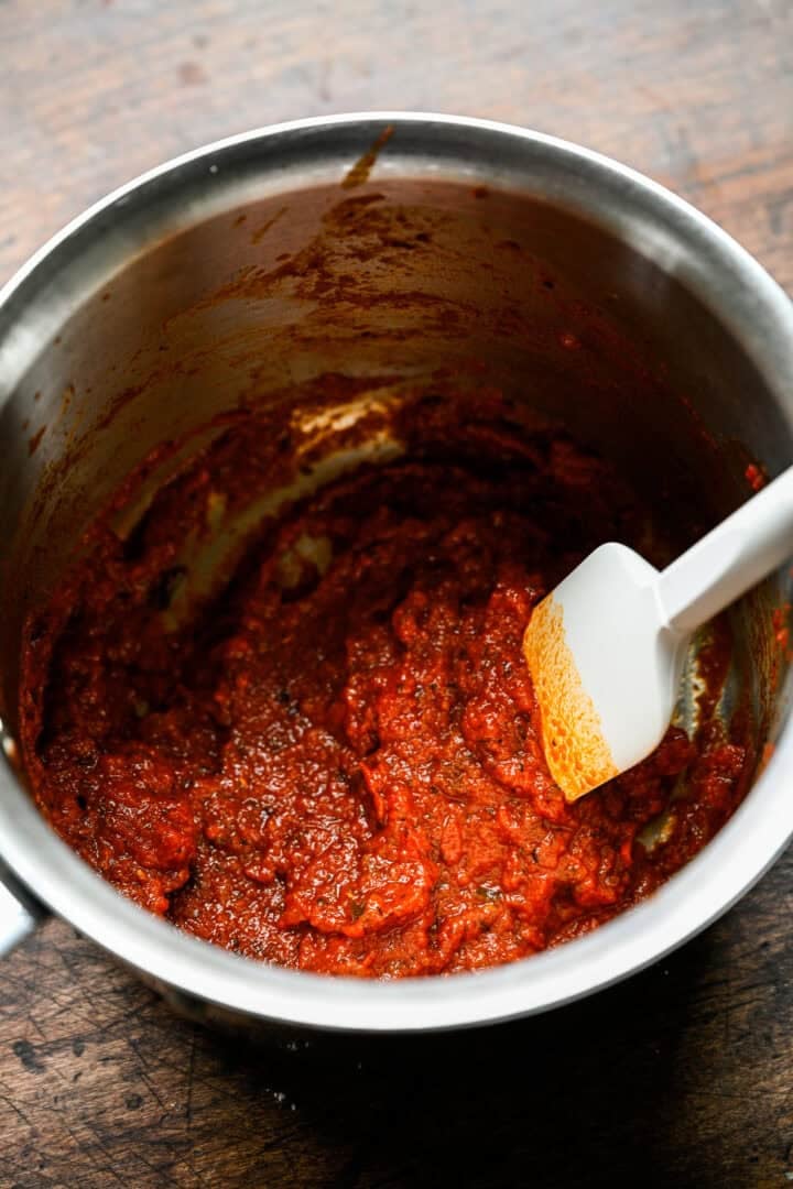 Pizza sauce cooked down to a thick paste in a saucepan, with a spatula dragged through it.