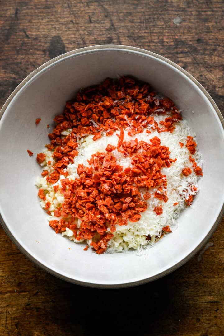 Chopped mozzarella, grated parmesan and finely chopped pepperoni in a mixing bowl before stirring.