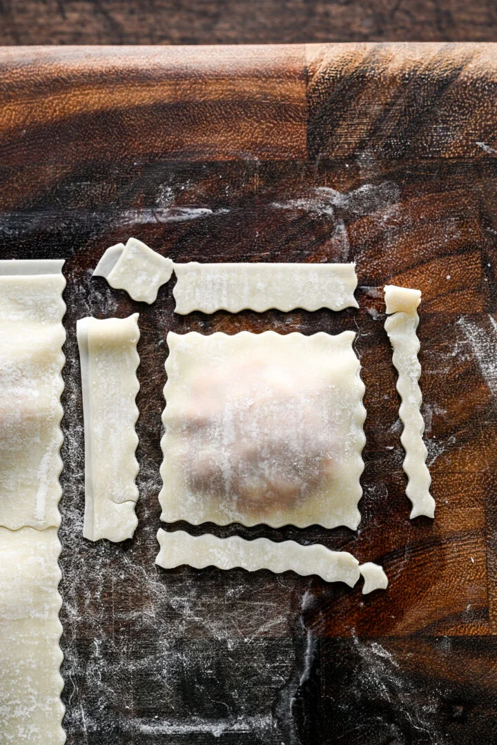 One uncooked pizza roll trimmed on all four sides, with strips of extra wrapper around it on a wooden cutting board.