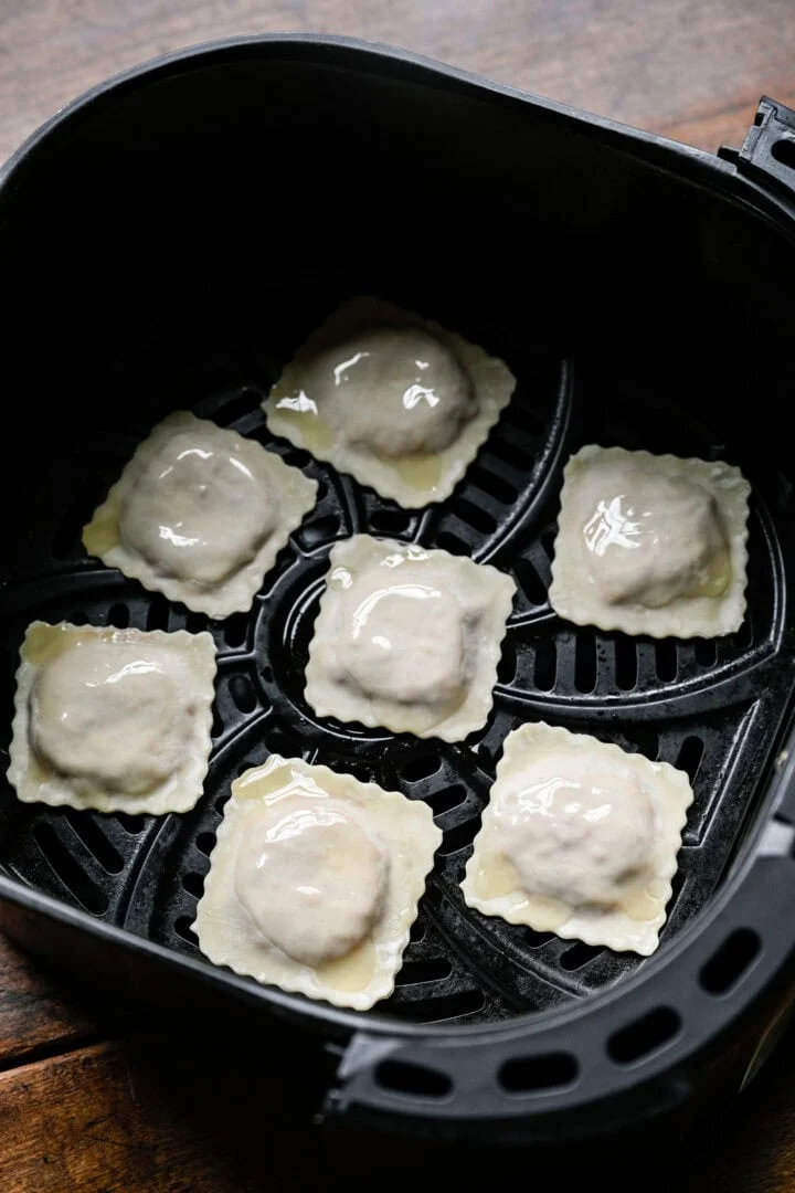 Seven uncooked pizza rolls brushed with oil in a single layer in an air fryer basket.