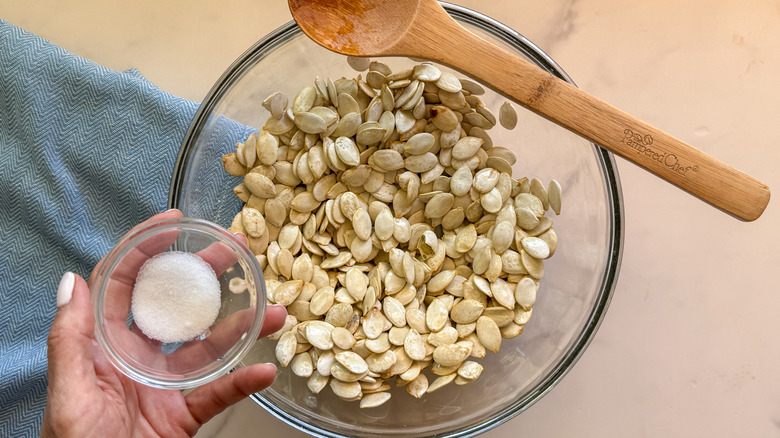 hand adding salt to bowl of pumpkin seeds