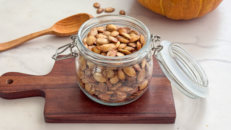 Jar of roasted pumpkin seeds on wooden board