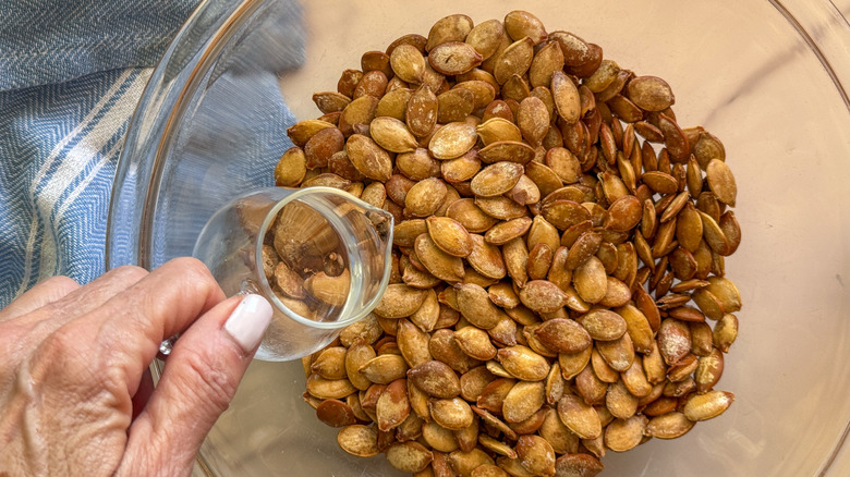 Hand pouring vinegar over roasted pumpkin seeds in bowl