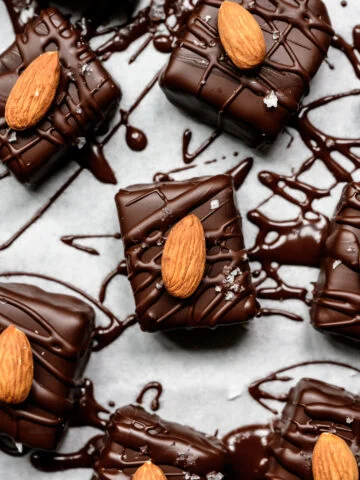 Close up view of chocolate coated bars topped with whole almonds and flaky salt on parchment.