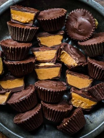 Overhead view of vegan peanut butter cups on a dark tray with some cut in half.